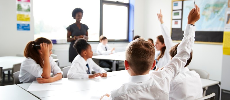 Come le famiglie vegane stanno ottenendo cambiamenti significativi nell'istruzione 3 High School Students Wearing Uniform Raising Hands To Answer Question Set By Teacher In Classroom