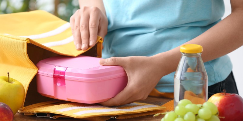 Woman packing fresh meal into lunch box bag in kitchen